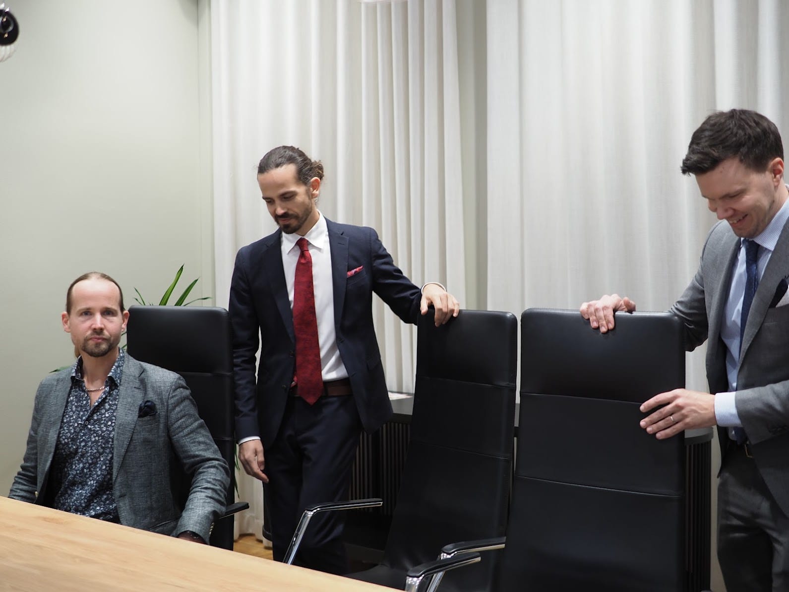 Kolme miestä pukee, istuvat kokoushuoneessa.