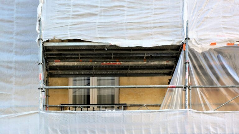 Rakennustelineet muovipeitteellä kerrostalon ikkunan edessä.